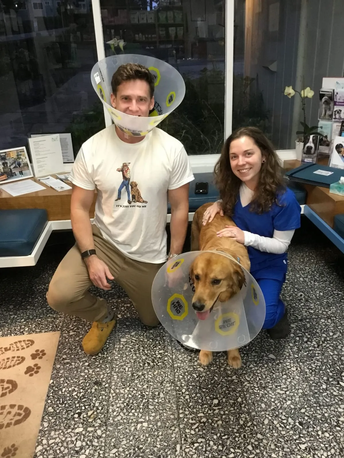 A man in a cone collar posing with a team member and a golden retriever in a cone