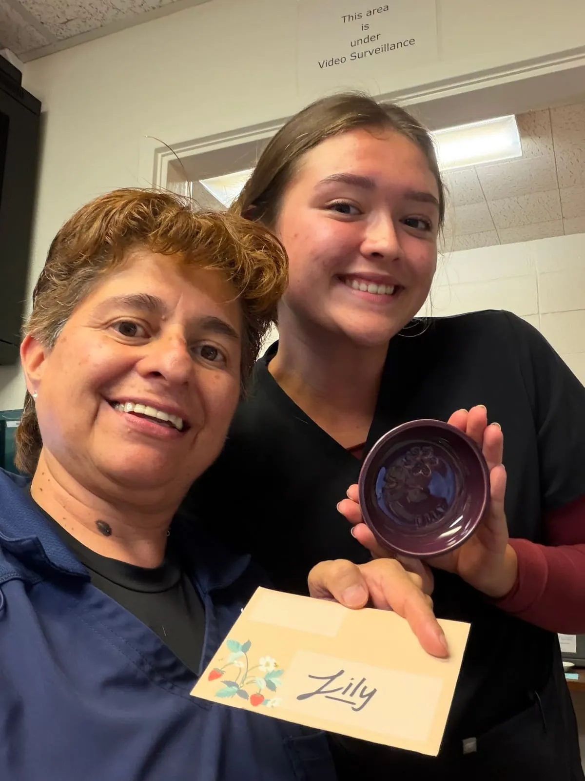 Two team members holding a clay paw print keepsake and a card for Lilly