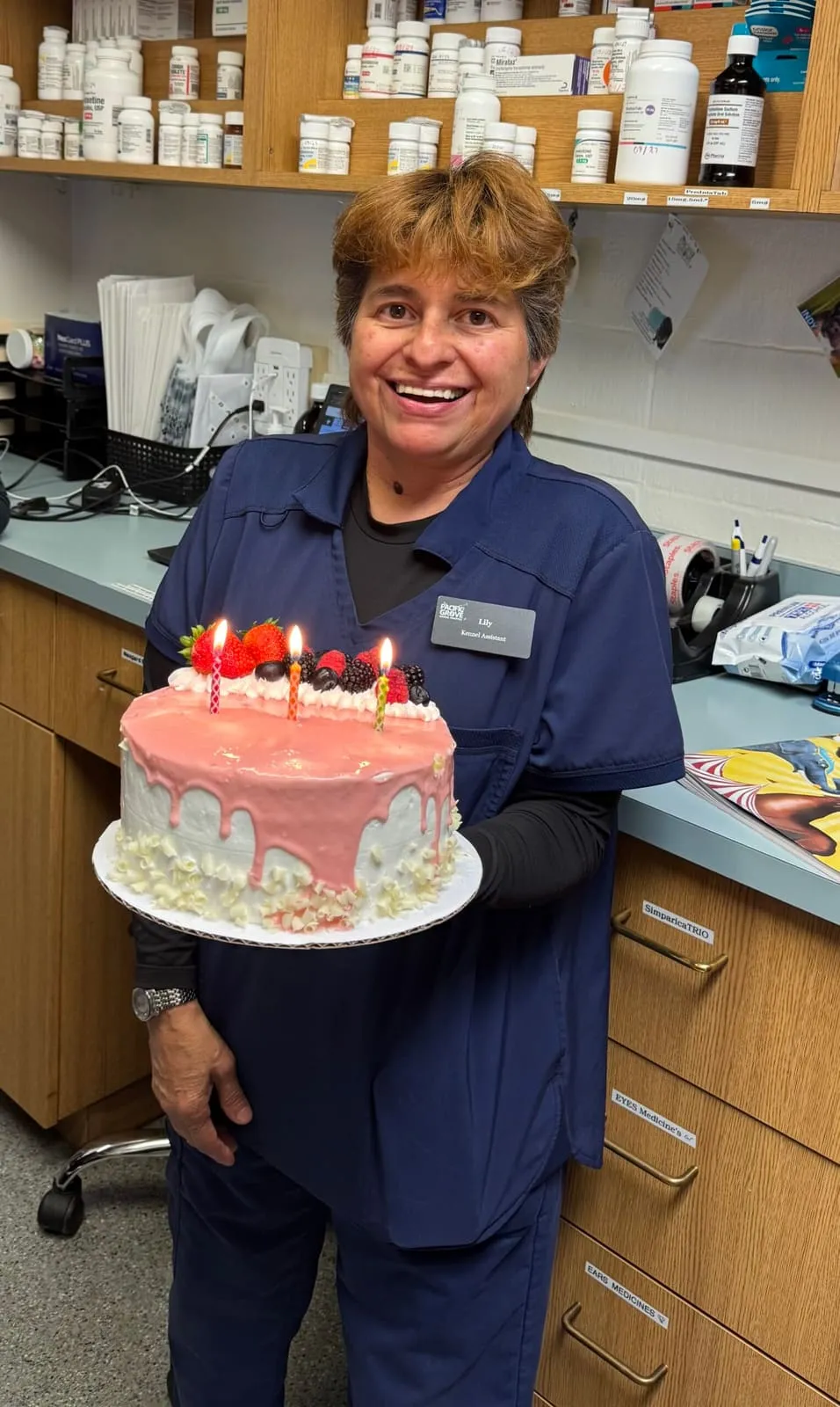 A team member holding a pink birthday cake with candles for Lily