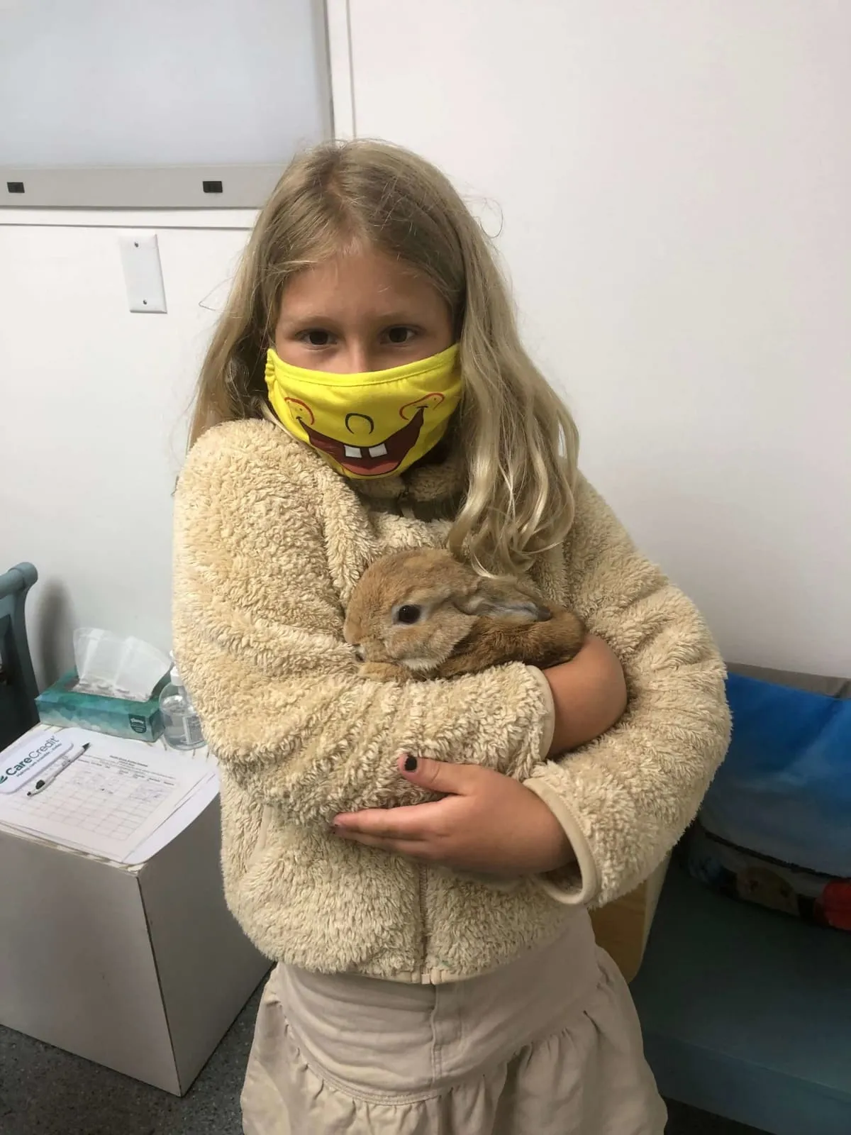 A girl in a mask holding Mr. Butters, a small rabbit