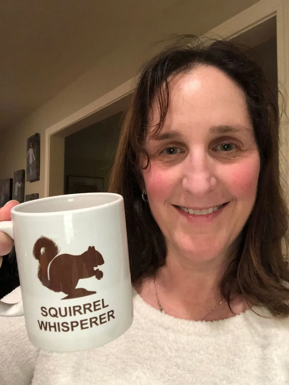 A smiling woman holding a Squirrel Whisperer mug